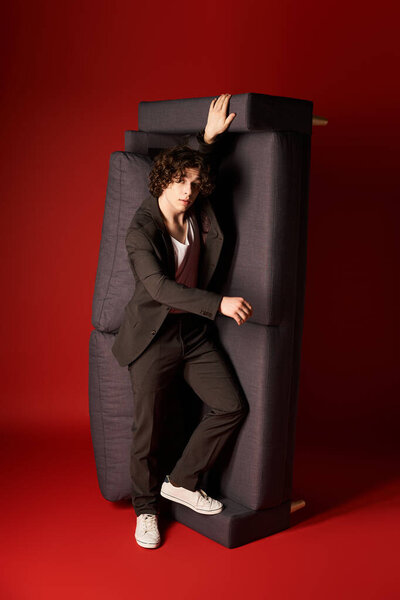 A young man with curly hair showcases a modern black outfit against a striking red backdrop.