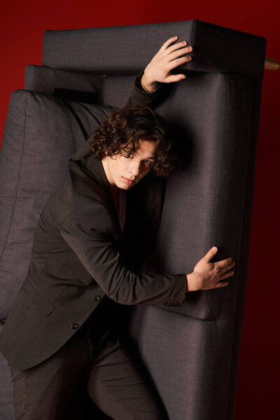 A young man with curly hair poses in fashionable black clothing, exuding confidence.