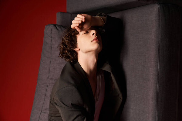In a contemporary studio, a young man with curly hair poses stylishly in black attire.