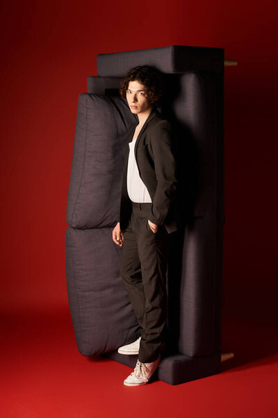 A stylish young man in sleek black attire stands confidently against a bold red backdrop.