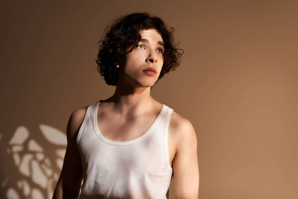 Молодой человек с вьющимися волосами носит майку в студии с мягким освещением.