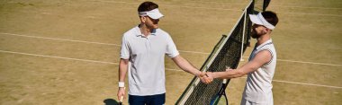 İki atletik adam, enerji dolu güneşli bir tenis kortunda oynanan dostça bir maç sonrasında el sıkışıyor.