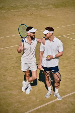 Eşcinsel çift, güneşin altında oynanan eğlenceli bir maçtan sonra tenis kortunda neşeli bir anı paylaşıyor..