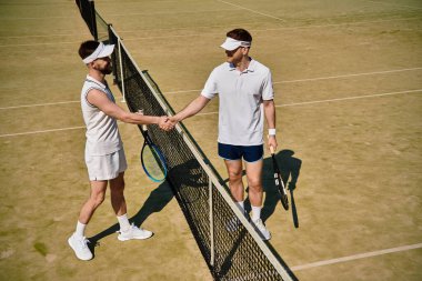 Tenis kortunda iki atletik adam güneşin altında oynanan dostça bir maçtan sonra el sıkışıyor..