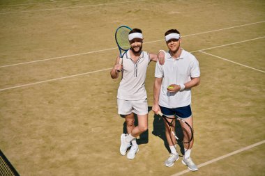 Güneşli bir yaz gününde tenis oynarken iki adam neşeli bir anı paylaşıyor..