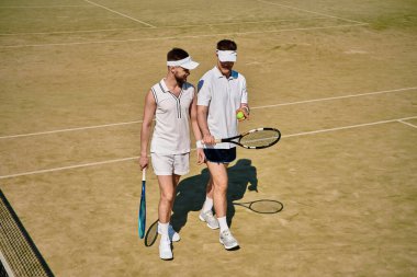 İki genç yazın güneşli bir kortta tenis oynarken keyifli bir anı paylaşıyor..
