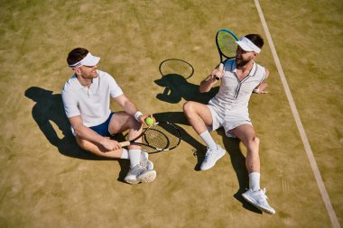 Yazın güneşli bir kortta tenis oynarken iki adam kahkahalarını paylaşıyor..