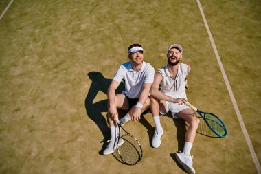 Tenis kortunda güneşli bir yaz gününün tadını çıkarırken iki adam kahkaha ve neşeyi paylaşıyor..