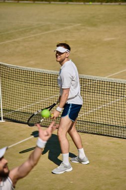 Beyaz spor giyimli yetenekli bir oyuncu yaz güneşinin altında tenis rallisine hazırlanıyor..