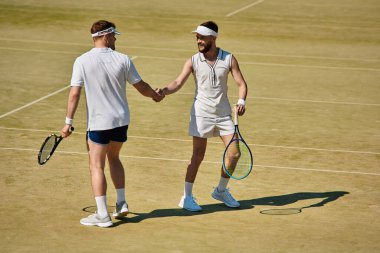 Tenis kortunda parlak bir gökyüzünün altında yapılan heyecanlı mitingden sonra iki atletik adam el sıkışıyor..