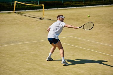 Yakışıklı bir adam sahada ustalıkla tenis oynarken yaz havası havayı dolduruyor..