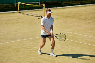 Kendini adamış bir oyuncu, beyaz spor kıyafetleriyle güneşli bir tenis kortunda yarışıyor..