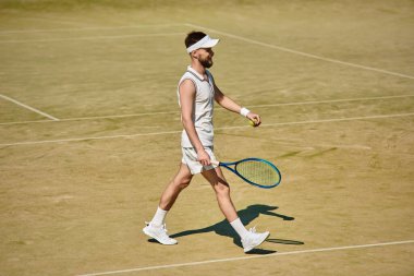 Yetenekli bir oyuncu, yaz tenis maçına çıkmaya hazır bir şekilde sahada güven içinde yürüyor..