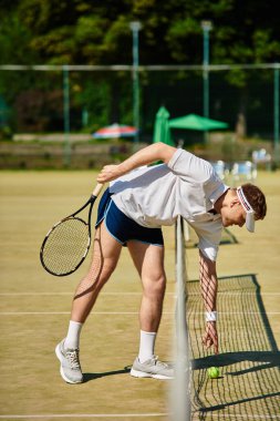 Yetenekli bir oyuncu, güneşli bir günde tenis topunu almak için eğilir..