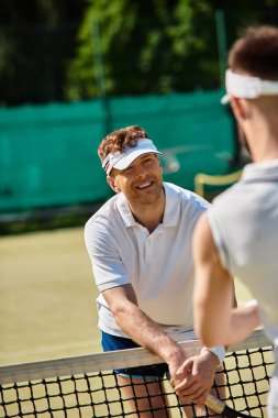 Genç eşcinsel çift güneşli bir yaz gününde tenis oynarken kahkaha ve eğlenceyi paylaşıyor.