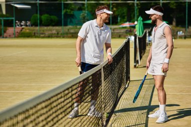Yazın güneşli bir kortta tenis oynarken iki adam neşeli bir anı paylaşıyor..