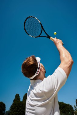 Beyaz giyimli yetenekli bir adam yazın canlı bir kortta yaklaşan tenis topuna nişan alır..