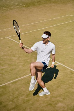 Yakışıklı adam, güneşli sahada tenis oynarken kazandığı atışı kutluyor..