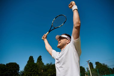 Beyaz spor kıyafetli yakışıklı bir adam yazın tenis zaferini sevinçle kutluyor..