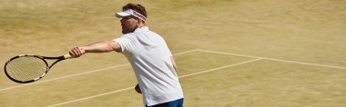 Yetenekli bir oyuncu, beyaz spor giyim ve afiş giyerken güneşli bir kortta tenis maharetini sergiliyor.
