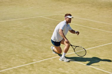 Yetenekli bir oyuncu, beyaz kıyafetlerle bir yaz günü tenis oynarken atletik hünerlerini sergiler..