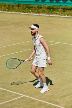 Parlak beyaz giyimli yetenekli bir oyuncu tenis kortunda yaz güneşinin altında hizmet etmeye hazırlanıyor..
