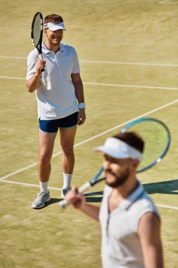 İki genç adam güneşli bir kortta tenis oynuyorlar, eğleniyorlar ve gülüyorlar..