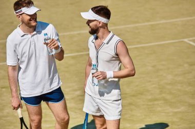 Güneşli bir günde, heyecan verici tenis maçlarında susuz kalmadan iki erkek aynı kahkahayı paylaşıyor..
