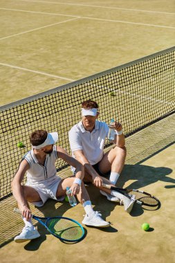 İki yakışıklı adam mola veriyor, su içip güneşli tenis gününün tadını çıkarıyorlar..