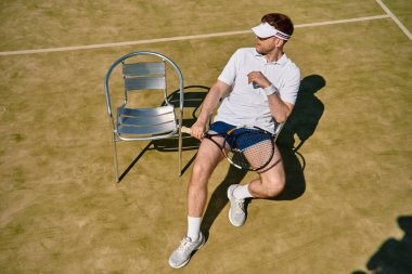 Beyaz spor giyimli enerjik bir adam yaz boyunca güneşli bir kortta tenis oynar..