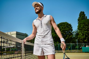 Gülümseyen beyaz giysili genç adam, yaz tenis kortuna hükmediyor..