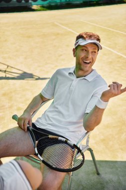 Beyaz takım elbiseli yakışıklı bir adam yoğun bir yaz tenis maçında mola veriyor..