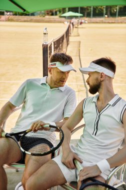Güneşli bir günde tenis kortunda dinlenirken iki adam aynı neşeli anı paylaşıyor..