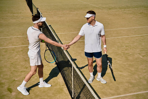 Двое опытных мужчин пожимают друг другу руки после напряженного теннисного матча в солнечный день.