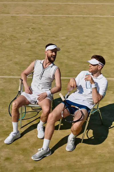 İki genç adam, yaz güneşinin altında oynadıkları heyecan verici tenis maçından sonra kahkahalarını paylaşıyorlar..