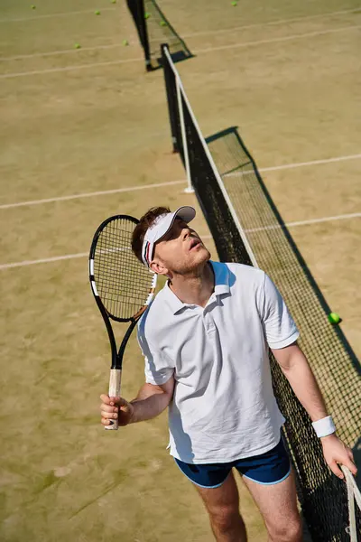 Parlak güneş ışığı, açık havada tenis oynarken beyaz spor giysili yakışıklı bir adamı aydınlatıyor..