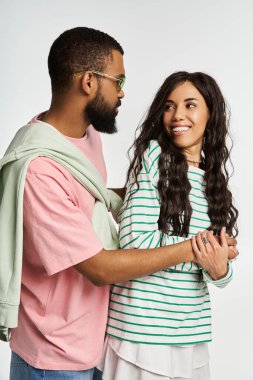 Çiftler birbirlerine gülümserken kucaklaşıyorlar, parlak bir ortamda moda kıyafetlerini sergiliyorlar..