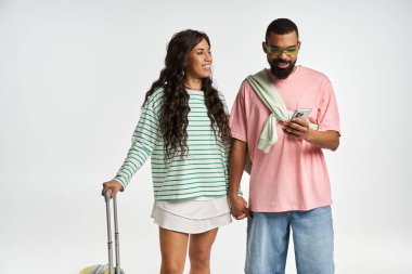 Tarz sahibi bir çift birbirlerine gülümsüyor, el ele tutuşuyorlar ve rahat bir yerde telefonlarını kontrol ediyorlar..