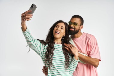 Bir erkek ve bir kadın neşeyle selfie çekerken moda kıyafetlerini içeride sergiliyorlar..