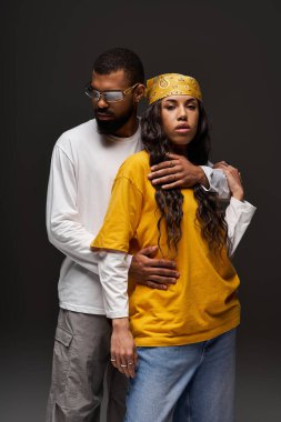 Moda bir çift yakın duruyor, çağdaş bir arkaplanda stil ve şefkat yayıyorlar..