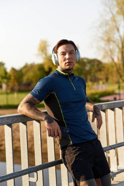 Atletik giyinmiş yakışıklı genç adam dışarıda müzik dinlerken rahatça dolaşır..
