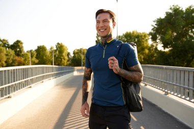 Genç bir adam huzur içinde huzurlu bir yolda yürüyor, gülümsüyor ve sıcak güneş ışığını kucaklıyor..