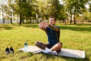 Yakışıklı genç adam sabahları yeşil bir parkta yoga minderinde sakince esniyor..