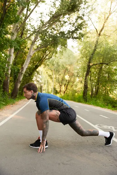 Yakışıklı bir genç adam ağaçlarla çevrili huzurlu bir sokakta gerilip koşmaya hazırlanıyor..