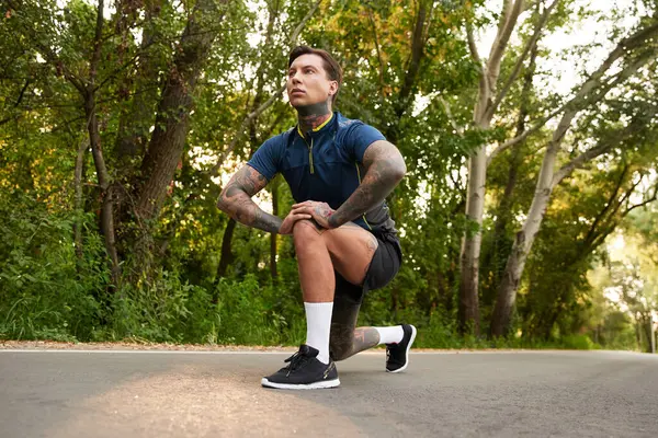 Genç bir adam yürüyüşü sırasında duraklıyor, yeşil bir yolda diz çöküyor..