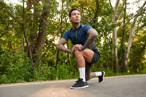 Genç, atletik bir adam yemyeşil çimenlikte sakin bir yürüyüş yaparken esnemek için durur..