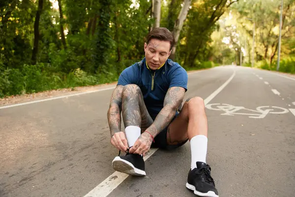 Yakışıklı genç adam yürüyüş sırasında ağaçlarla çevrili sessiz bir sokakta ayakkabılarını bağlamak için durur..