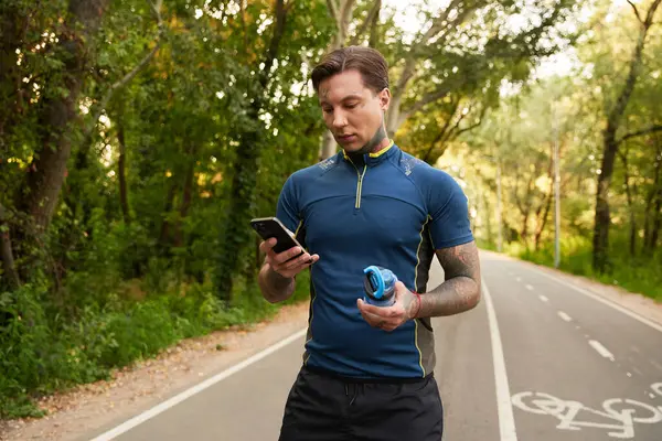 Yakışıklı genç adam, akıllı telefonuyla meşgul bir şekilde ağaçlık bir patikada geziniyor..