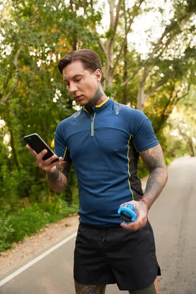 Yakışıklı bir genç adam, güzel bir yeşilliğin ortasında telefonuna odaklanarak yürüyüşünü durdurur..