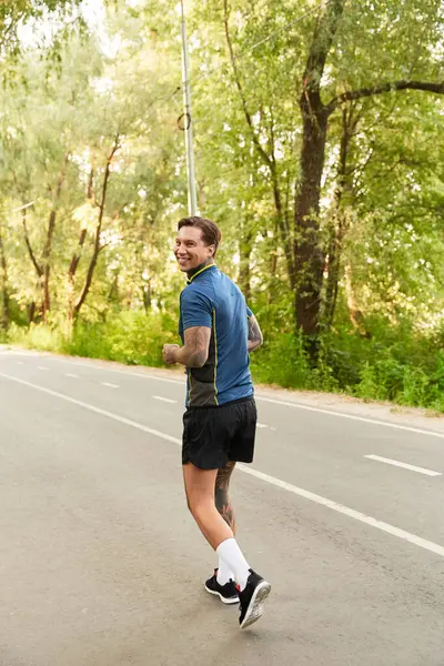 Yakışıklı genç adam yemyeşil ve güneş ışığıyla çevrili manzaralı bir yolda mutlu bir şekilde yürüyor..